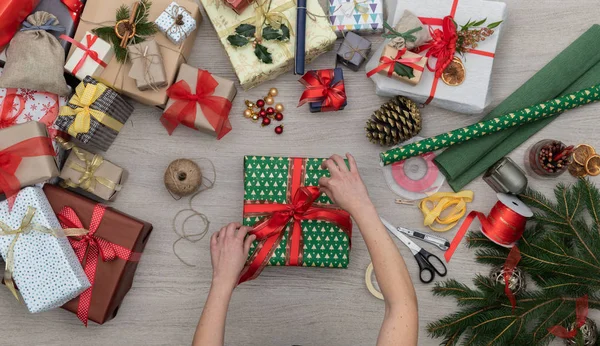 Χέρια προετοιμασία παρόντες κουτί δώρου σε κάθετη προβολή επάνω ξύλινο τραπέζι γεμάτο δώρα Χριστουγέννων παρουσιάζει, εργαλεία πεύκα και χειροτεχνίας. Χριστούγεννα χειμώνα διακοπές σεζόν κόμμα άνθρωποι κοινωνικής media κάρτα φόντο — Φωτογραφία Αρχείου