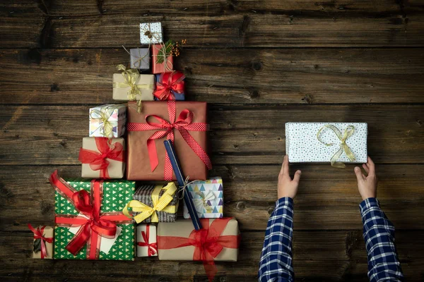 Τα χέρια με το παρόν δώρων κουτί σε κάθετη προβολή επάνω σκούρο ξύλο εκλεκτής ποιότητας με Χριστουγεννιάτικο δέντρο πεύκο από παρόντες κουτιά δώρων. Κοινωνική media σεζόν διακοπών χειμώνα Χριστούγεννα κόμμα κάρτα φόντο, πορτρέτο ιστορία — Φωτογραφία Αρχείου
