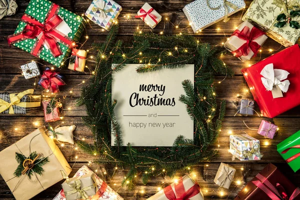 Καλά Χριστούγεννα και Ευτυχισμένο το νέο έτος χαιρετισμούς σε κάθετη προβολή επάνω εκλεκτής ποιότητας ξύλο. Pine κλαδιά, κορδέλες, φώτα, παρόντες κουτιά διακοσμημένα πλαίσιο δώρο. Χριστούγεννα χειμερινές διακοπές σεζόν κοινωνικής media κάρτα φόντο — Φωτογραφία Αρχείου