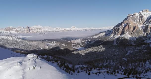 Backward aerial to snowy valley with woods forest and road at Valparola pass.Sunny sunset or sunrise, clear sky.Winter Dolomites Italian Alps mountains outdoor nature establishment isher.4k drone flight — стоковое видео