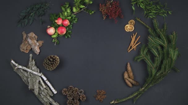 Les mains de la personne aérienne mettant guirlande sur l'espace de copie de texte.Vue verticale du dessus de la table sombre avec des feuilles naturelles, des cônes de pin, de l'écorce, de la grenade. — Video