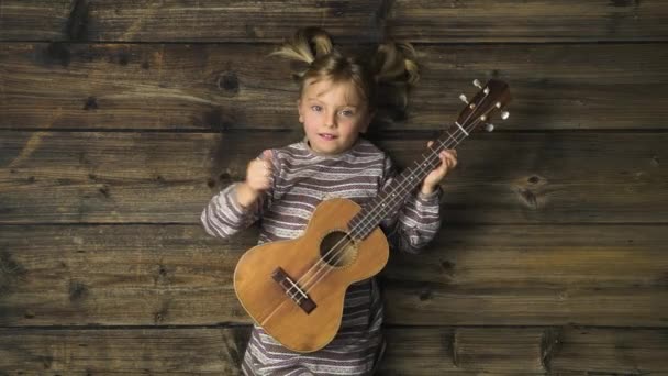 Overhead menina feliz criança no fundo de madeira vintage jogando ukulele guitarri.Text ou logotipo cópia space.Vertical top view.Social cartão para feriado de Natal season.4k vídeo — Vídeo de Stock