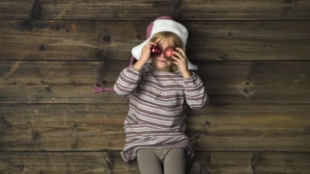头顶愉快的微笑的孩子女孩与帽子玩装饰在复古木背景。文本或徽标复制空间。垂直顶部视图。圣诞节或冬季假期的社交卡. 4 k 视频 — 图库视频影像