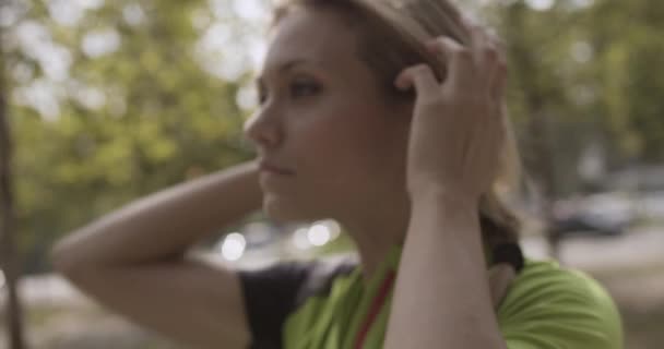 Mujer rubia joven en ropa de fitness ajustando el cabello para correr training.Summer día soleado.Ciudad verde industrial.Corredor urbano ejercicio de actividad cardio saludable.4k cámara lenta 60p video — Vídeos de Stock