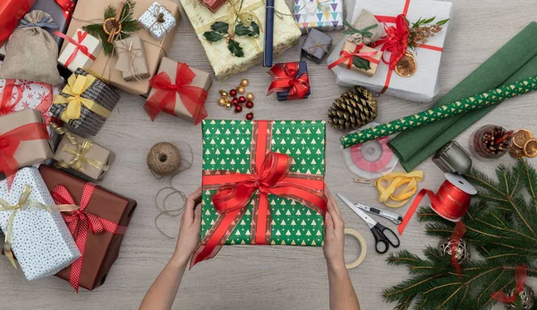 Händer förbereda nuvarande presentbox i vertikala ovanifrån trä presenterar bord fullt av julklappar, tall och hemslöjd verktyg. Xmas vintern semester säsong part människor social median kort bakgrund — Stockfoto