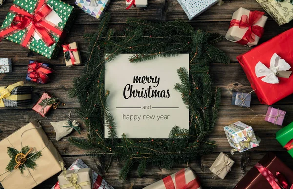 Καλά Χριστούγεννα και Ευτυχισμένο το νέο έτος χαιρετισμούς σε κάθετη προβολή επάνω εκλεκτής ποιότητας ξύλο. Pine κλαδιά, κορδέλες, φώτα, παρόντες κουτιά διακοσμημένα πλαίσιο δώρο. Χριστούγεννα χειμερινές διακοπές σεζόν κοινωνικής media κάρτα φόντο — Φωτογραφία Αρχείου