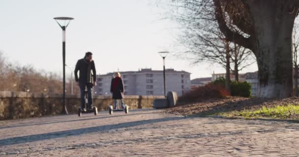 女儿的孩子女孩骑赛格威与她的爸爸在城市。现代未来运输技术。活跃的家庭。温暖的日落寒冷的天气回来. 4k 慢动作60p 视频 — 图库视频影像