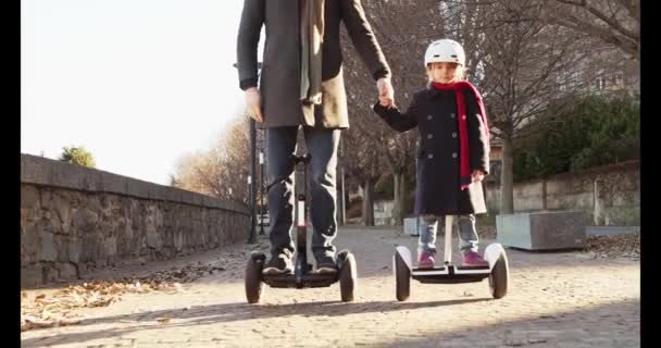 Hija niña montar segway con su padre en la ciudad.Tecnología de transporte futuro moderno.Active Family.Park acera urbana al aire libre.Warm puesta del sol frío backlight.4k cámara lenta 60p vídeo frontal — Vídeos de Stock