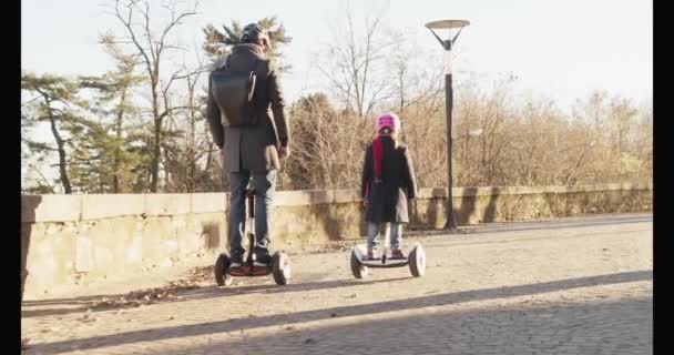 Daughter child girl riding segway with her dad in city.Modern future transport technology.Active Family.Park sidewalk urban outdoor.Warm sunset cold weather backlight.4k slow motion 60p back video — Stock Video