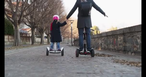 A dcera dítě dívka na koni segway s jejím otcem v městě. Moderní budoucí dopravní technologie. Aktivní Family.Park chodníku městské venkovní. Teplé slunce chladné počasí backlight.4k zpomalené video 60p — Stock video