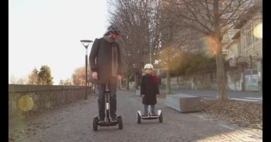 Kız kız çocuk babası şehirde Segway sürme. Modern gelecekteki ulaşım teknolojisi. Active Family.Park kaldırım kentsel açık. Sıcak gün batımı soğuk hava backlight.4k ağır çekim 60p açık video