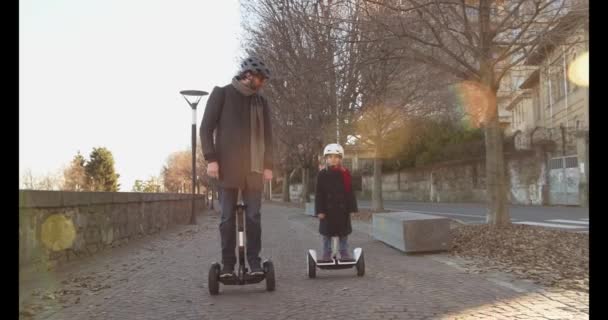 Daughter child girl riding segway with her dad in city.Modern future transport technology.Active Family.Park sidewalk urban outdoor.Warm sunset cold weather backlight.4k slow motion 60p front video — Stock Video