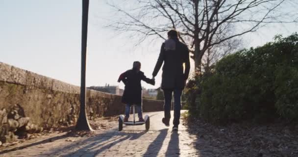 Daughter child girl learning segway riding with dad teaching in city.Modern future transport technology.Active safety family.Sidewalk urban outdoor.Warm sunset cold backlight.4k slow motion 60p video — Stock Video