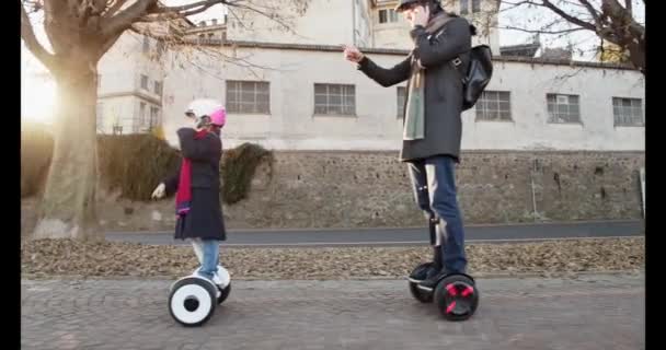 Daughter child girl calling with mobile phone riding segway with her dad in city.Modern future transport technology.Active Family.Urban outdoor.Cold weather backlight.4k slow motion 60p side video — 비디오