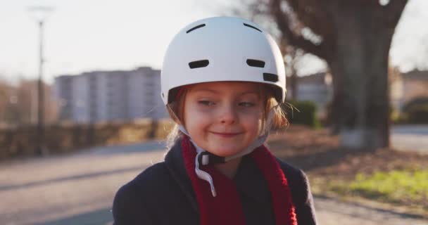 Happy usmívající se dcera dítě dívka, která nosí bezpečnostní Helma jízdní kolo portrét v městském parku. Dětství, aktivní, bezpečnostní koncepty. Chodníku městské venkovní. Teplé slunce backlight.4k slow motion videa — Stock video