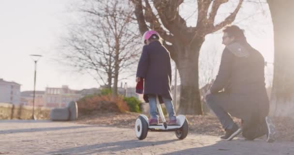 Daughter child girl learning segway riding with dad teaching in city.Modern future transport technology.Active safety family.Sidewalk urban outdoor.Warm sunset cold backlight.4k slow motion 60p video — Stock Video