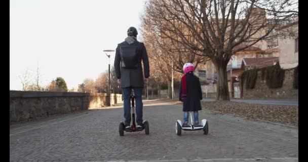 Córka dziecko dziewczynka jazda segway z tatą w mieście. Nowoczesny transport przyszłych technologii. Active Family.Park chodnik miejski odkryty. Zachód słońca zimnej pogodzie backlight.4k zwolnionym tempie 60p wideo — Wideo stockowe