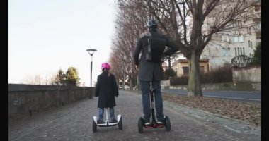Kız kız çocuk babası şehirde Segway sürme. Modern gelecekteki ulaşım teknolojisi. Active Family.Park kaldırım kentsel açık. Sıcak gün batımı soğuk hava backlight.4k ağır çekim 60p video