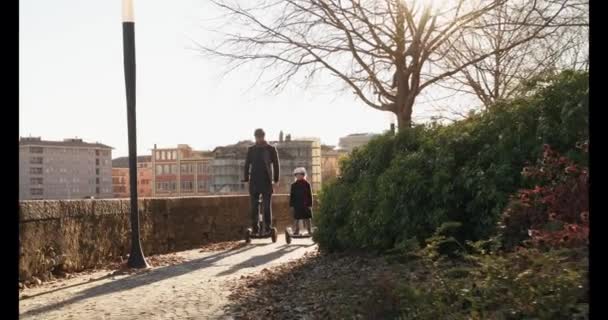 Figlia bambina cavalcando segway con il padre in città.Moderna tecnologia di trasporto futuro.Famiglia attiva.Parco marciapiede urbano all'aperto.Caldo tramonto freddo retroilluminazione.4k rallentatore 60p video anteriore — Video Stock