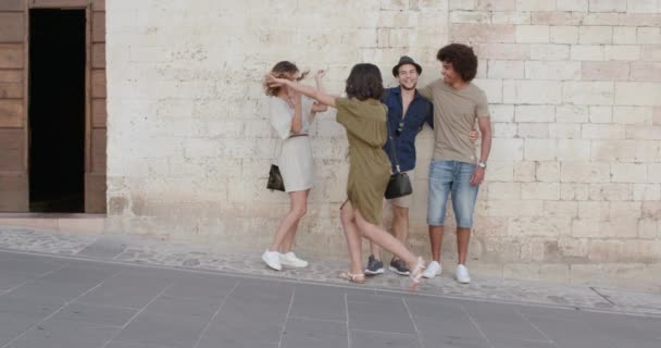 Négy boldog turista emberek barátai pózol, mosolyogva és a szórakozás közel egy téglafal a vidéki város Spello. Friends olasz kirándulás Umbria. 4k lassú mozgás — Stock videók