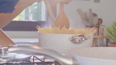adam kaynar su tenceresinde spagetti makarna karıştırma. Genç insanlar çift yemek ve yemek hazırlama, öğle veya akşam yemeği için spagetti makarna carbonara yemek modern ev açık alan mutfakta.