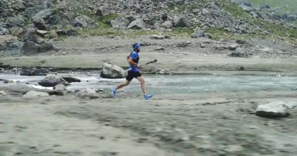 Чоловік біжить поблизу гірського струмка річки. Залізничний бігун біжить на вершину піку тренування на скелястому сходженні. Дика зелена природа на відкритому повітрі в похмуру туманну погоду. Діяльність, спорт, ефект, виклик, концепції сили волі — стокове відео