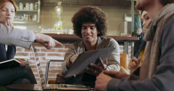 Мужчина беседует с коллегами и клиентами с ноутбуком и таблицей. Группа мультиэтнических людей, имеющих неформальную деловую команду, встречается в ресторанном салоне. — стоковое видео