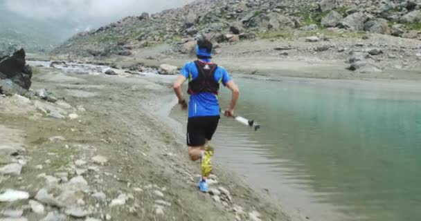 山の小川の近くを走っている男トレイルランナーは、岩の登りでトップピークトレーニングに走ります。曇り霧の悪天候で屋外野生の緑の自然。活動、スポーツ、努力、挑戦、意志の概念 — ストック動画