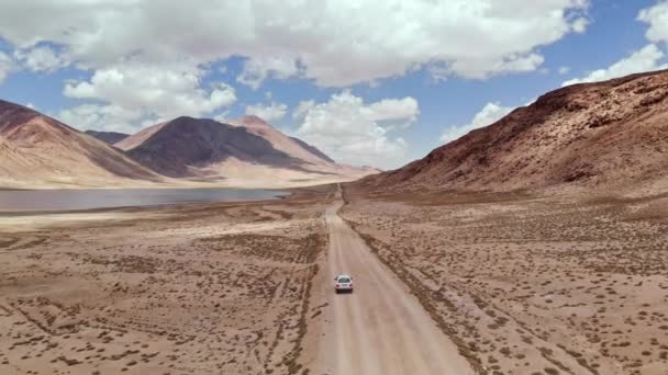 乾燥した砂漠の山の近くの砂利道の道に沿って運転オフロード4x4 の車の上に空中。パミールはキルギスとタジキスタンの砂漠、中央アジアで高速道路シルクロードの旅の冒険をしました。4k ドローンフライトビデオ — ストック動画