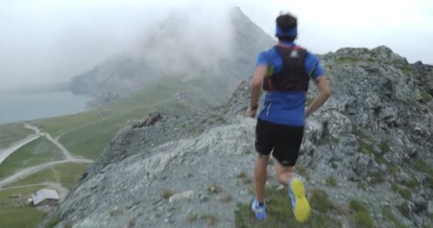 人跑在悬崖边上。越野赛跑者跑向山顶，在岩石攀爬上训练。野生绿色自然户外在多云和多雾的恶劣天气。活动、运动、努力、挑战、意志力概念 — 图库视频影像