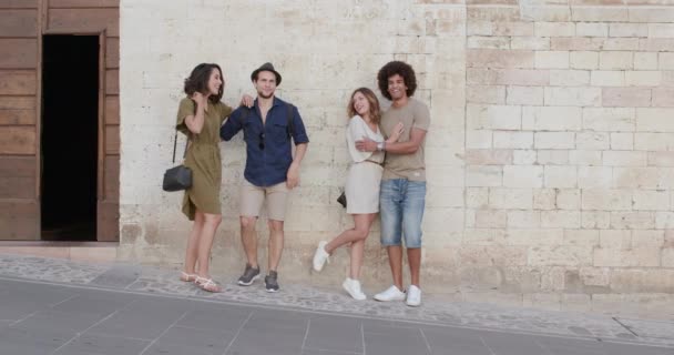 Cuatro felices turistas amigos posando, sonriendo y divirtiéndose cerca de una pared de ladrillo en la ciudad rural de Spello.Amigos viaje italiano en Umbría.4k cámara lenta — Vídeo de stock