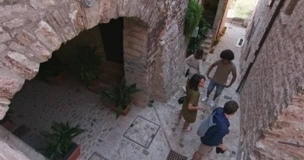 Quatro pessoas turísticas felizes andando e correndo pela pequena rua visitando a cidade rural de Spello.Top vista elevada.Amigos viagem de férias italiano em Umbria.4k câmera lenta — Vídeo de Stock