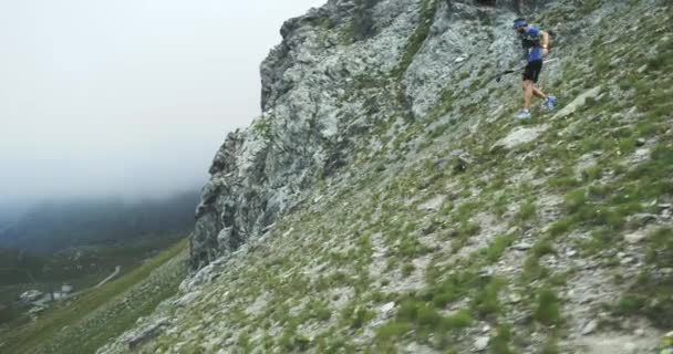 Man descending run on mountain slope.Trail runner running to top peak training on rocky climb.Wild green nature outdoors in cloudy foggy bad weather. Activity,sport,effort,challenge,willpower concepts — Stock Video