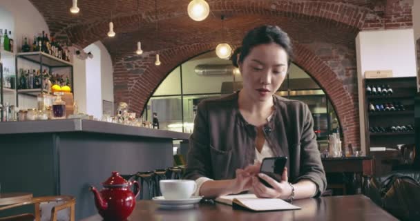 Жінка п'є чай за допомогою смартфона mobile.Front випадковий одягнений азіатський китайський, ділова жінка працює в бізнесі або навчається в кафе, ресторані лаунж або кафетерії. Модерн, коворкінг, різноманітність, багатоетнічний — стокове відео