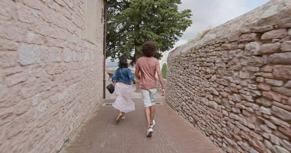 Romantic couple walking visiting happy rural town of Assisi.Back follow.Friends italian trip in Umbria.4k slow motion