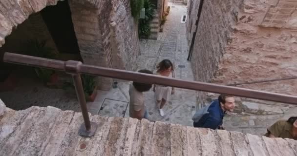 Cuatro personas turísticas felices caminando y corriendo por la pequeña calle visitando la ciudad rural de Spello.Top vista alta.Amigos viaje de vacaciones italiano en Umbria.4k cámara lenta — Vídeo de stock