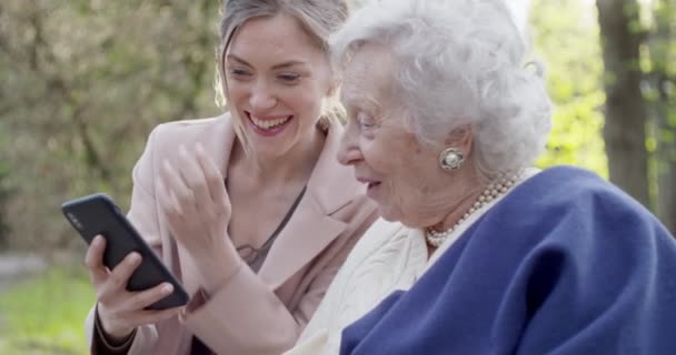 Femme et grand-mère aînée utilisant un appareil smartphone au park.Petite-fille et grand-mère parler avec mobile.Active, attentionné, affectueux gens relationship.slow motion vidéo — Video