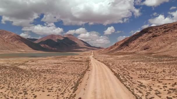 在阳光明媚的日子里, 在干旱的沙漠山脉附近的公路小道上的砾石上空中飞行。帕米尔高速公路丝绸之路旅行冒险在吉尔吉斯斯坦和塔吉克斯坦沙漠, 中亚. 4k 无人机飞行建立者视频 — 图库视频影像