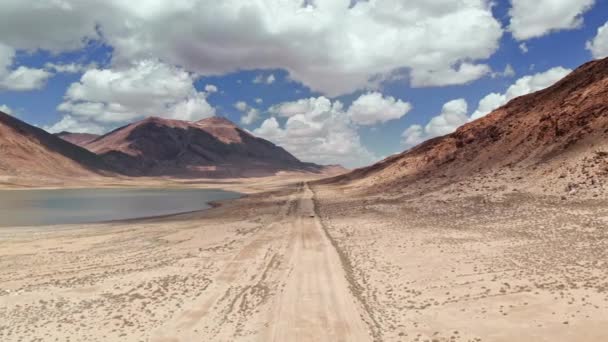 Εναέρια πάνω από το δρόμο 4x4 αυτοκίνητο οδήγηση κατά μήκος χαλίκι μονοπάτι δρόμο κοντά σε ξηρά βουνά έρημο. Pamir αυτοκινητόδρομος μεταξωτή εκδρομή στο Κιργιστάν και στην έρημο του Τατζικιστάν, στην Κεντρική Ασία. 4K τηλεκατευθυνόμενο βίντεο πτήσης — Αρχείο Βίντεο