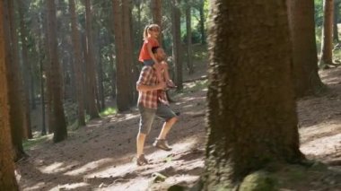 Ormanda yürüyen kızına domuz sırtı süren babanın yan görüntüsü. Baba, orman yolu boyunca yürüyüş omuzlarında kızı tutan. Baba ve kızı birlikte orman yolunda yürüyüş