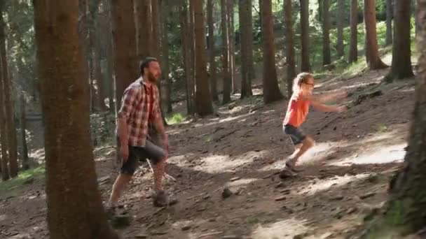 Šťastná rodina otce a dcery, jak kráčí po kopci mezi borovicemi na venkově. Dívka, která kráčí před otcem na horské stezce. Otec a dcera jsou na cestě lesem. Slunečný den, podsvícení — Stock video
