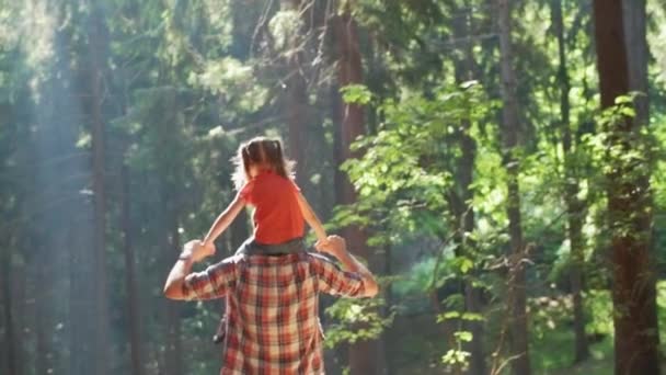 Tillbaka syn på far som ger en piggyback rida till dotter promenader i skogen. Fader Holding dotter på skuldror vandring längs skogsstigen väg. Far och dotter vandra på skogsstigen tillsammans — Stockvideo