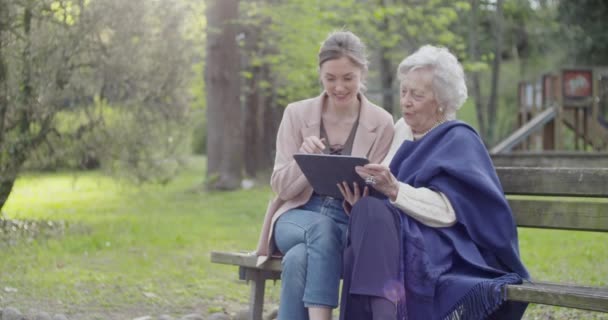 여자와 노인 할머니공원에서 화상 통화를 위해 태블릿 장치를 사용. 손녀와 할머니는 모바일과 함께 이야기. 활동적이고, 배려심이 많고, 사랑하는 사람들의 관계.슬로우 모션 비디오 — 비디오