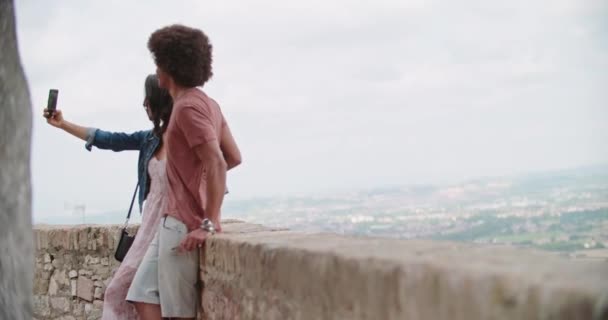 Romantic couple taking a selfie with smartphone in rural town of Assisi.approach wide shot.Friends italian trip in Umbria.4k slow motion — Stock Video