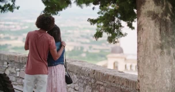 Vista trasera de pareja romántica abrazándose mirando al mirador en la ciudad rural de Assi.Portrait medio shot.Friends viaje italiano en Umbria.4k cámara lenta — Vídeo de stock