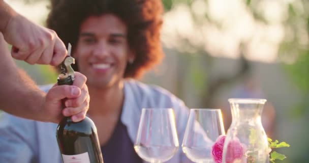 Camarero abrir la botella de vino y verter vino tinto en vaso mientras la gente, hablando, comiendo, bebiendo durante la cena gourmet romántica reunión al atardecer. — Vídeos de Stock