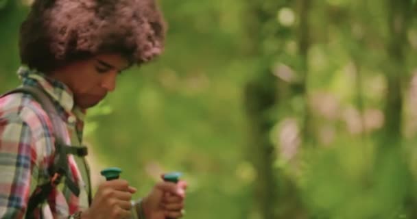 Άνθρωπος και γυναίκα πεζοπορία χρησιμοποιώντας πόλους πεζοπορίας μέσα από το δάσος το καλοκαίρι ηλιόλουστη μέρα. Περιπατητές στο Μάουντεν. Αργή κίνηση 60 fps μπροστινό χέρι που διατηρούνται — Αρχείο Βίντεο