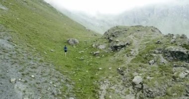 Dağ da koşan bir adamın anteni. Patika koşucusu kayalık tırmanışta en tepeye doğru koşuyor. Bulutlu sisli kötü havalarda vahşi yeşil doğa açık havada. Aktivite, spor, çaba, meydan okuma, irade.