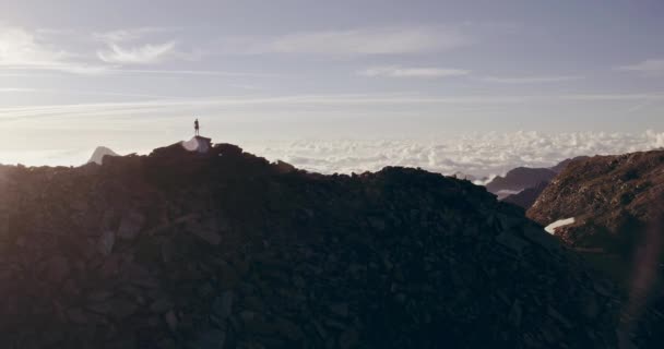 Pista aérea corredor hombre de pie en la cima de la montaña objetivo mirando horizonte view.drone shot.Wild naturaleza al aire libre al amanecer o al atardecer backlit.Training actividad, deporte, esfuerzo, desafío, conceptos de fuerza de voluntad — Vídeo de stock