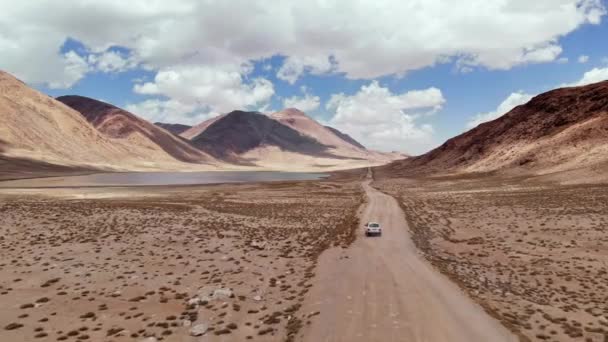 Aerial over off road 4x4 car driving along gravel trail path near arid desert mountains.Pamir Highway silk road trip adventure in Kyrgyzstan and Tajikistan desert,central Asia.4k drone flight video — Stock Video